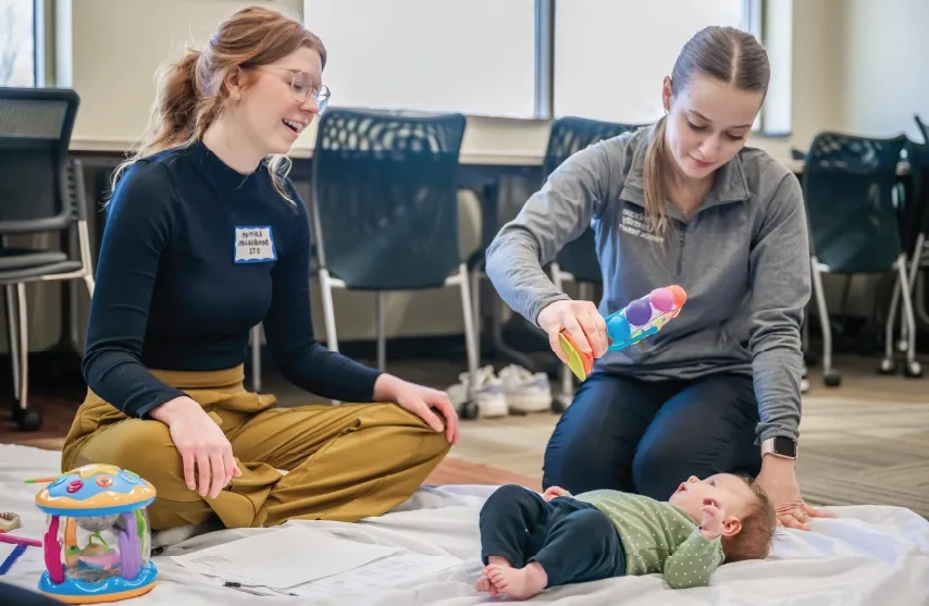 Physical therapist assesses young patient in pediatrics lab with parent nearby.